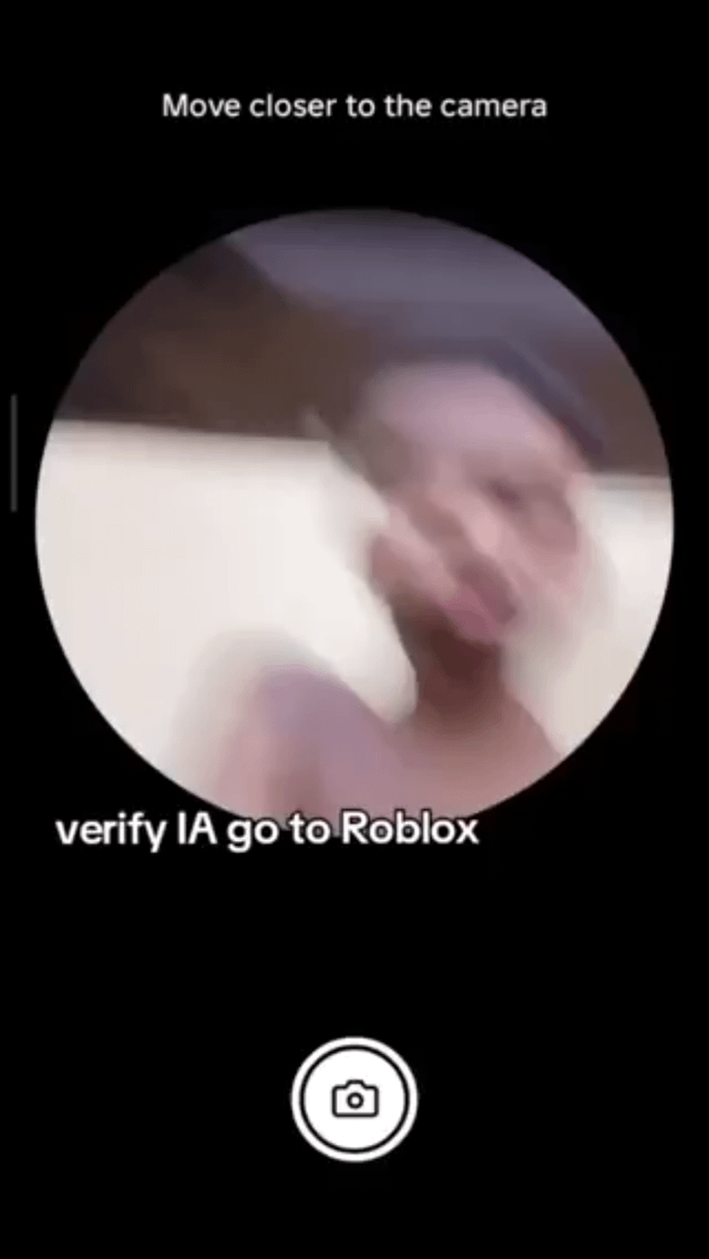 A meme depicting the frustration of attempting to verify one's identity to play Roblox. The image features a black background with a circular, blurred photograph of a person's upper body and face at the center, suggesting motion (likely from moving closer to a camera). Above the circle, white text reads 'Move closer to the camera,' and below it, white text states 'verify IA go to Roblox' (possibly containing a typo, likely intended to mean 'verify to go to Roblox'). The blurred facial features emphasize the struggle or absurdity of the verification process, humorously capturing the common user experience of encountering hurdles when trying to access the game.