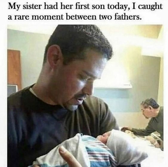The image depicts a heartwarming real-life moment featuring two fathers and a newborn baby. In the foreground, a man holds a swaddled newborn baby, gazing down at the infant with a tender and focused expression. The baby is wrapped in a striped blanket with a white cap. In the background, another man is seated, looking attentively towards the baby and the father holding it. The text at the top of the image explains the context: the sister's first son was born, capturing a rare moment between two fathers (likely the new father and grandfather).