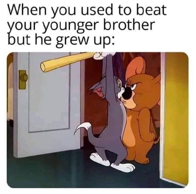 This is a relatable humor meme. The top of the image has text that reads 'When you used to beat your younger brother but he grew up:'. Below the text is a screenshot from the classic animated series *Tom and Jerry*: Tom the cat is standing in a doorway holding a wooden baseball bat raised over his head as if he intended to attack, but he is pressed up against a much larger, buff, angry mouse (Muscles, Jerry's cousin) who is staring menacingly at Tom. The scene humorously illustrates the role reversal when a smaller, previously picked-on younger sibling grows bigger and stronger than the older sibling who used to bully them.