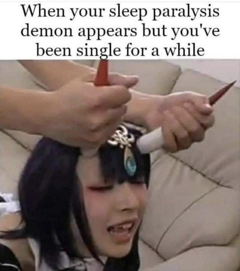 The meme consists of a top text overlay reading 'When your sleep paralysis demon appears but you've been single for a while' above an image of a person with dark hair wearing a decorative headpiece featuring a blue gem. Another individual's hands are visible styling the person's hair with red hair tools. The humor arises from the juxtaposition of the typically frightening concept of a 'sleep paralysis demon' with the relatable experience of loneliness from being single, implying the 'demon' is welcomed as attention.