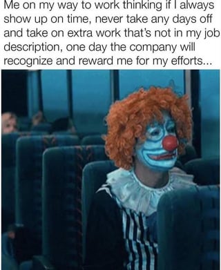 The image features a clown with orange hair, white face paint, a red nose, and a ruffled collar sitting in a public transport seat (likely a bus or train). The clown has a sad, resigned expression, looking forward. Above the clown is a text overlay representing the clown's internal monologue: 'Me on my way to work thinking if I always show up on time, never take any days off and take on extra work that's not in my job description, one day the company will recognize and reward me for my efforts...'. The humor stems from the irony of the 'clown' metaphor, implying that believing overworking will lead to recognition is foolish, as such efforts often go unrewarded in corporate environments.
