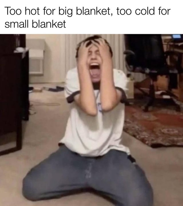 The meme depicts a person in a state of frustration, kneeling on the floor of a cluttered room. They are wearing a white t-shirt and blue jeans, with their hands covering their face and mouth open in a yell, conveying intense distress. Above the person, a text overlay reads 'Too hot for big blanket, too cold for small blanket,' highlighting the relatable daily struggle of finding the right blanket temperature for comfort, likely in the context of trying to sleep. The background includes a chair, desk, and scattered items, emphasizing a casual home environment.
