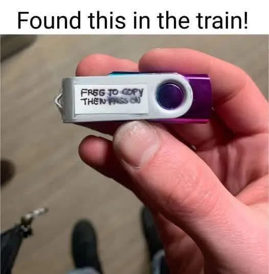 The image shows a person's hand holding a small purple and silver USB flash drive, which the poster says they found inside a train. Top text on the image reads "Found this in the train!". The USB has a handwritten white label that says "FREG TO COPY THEN PASS ON" (the first word is a misspelling, with a partial correction to make it "FREE"). The post's original title "Look safe" is an ironic joke referencing the common cybersecurity warning that plugging in random unknown USB drives found in public is unsafe, making the title tongue-in-cheek.