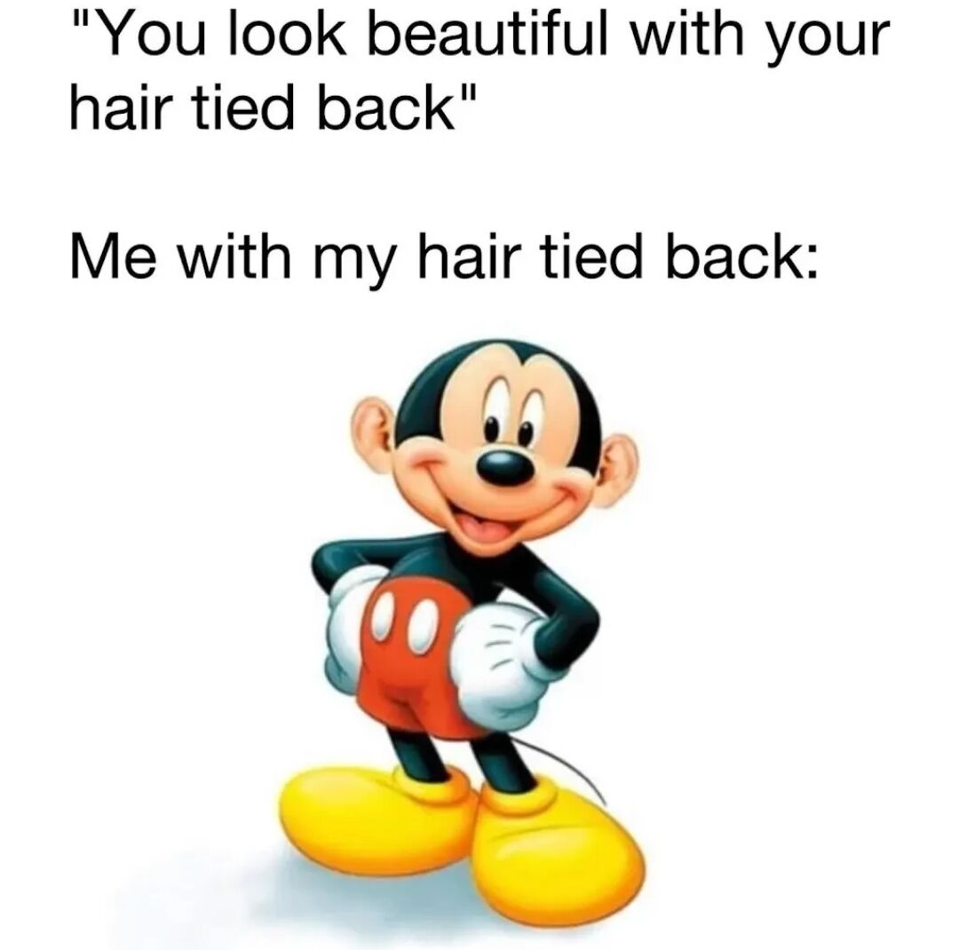 A meme featuring two sections of text and an animated character. The top text reads: "You look beautiful with your hair tied back" in quotation marks, suggesting a compliment. Below this, the text "Me with my hair tied back:" is followed by an image of Mickey Mouse, the iconic Disney character. Mickey is depicted with a cheerful, smiling expression, hands on his hips, and a confident stance, wearing his classic red shorts with white buttons, black上衣, and yellow shoes. The humor arises from the playful contrast between the sincere compliment and the lighthearted, self-assured reaction embodied by Mickey's upbeat demeanor, creating a relatable and wholesome joke about self-perception when receiving positive comments about appearance.