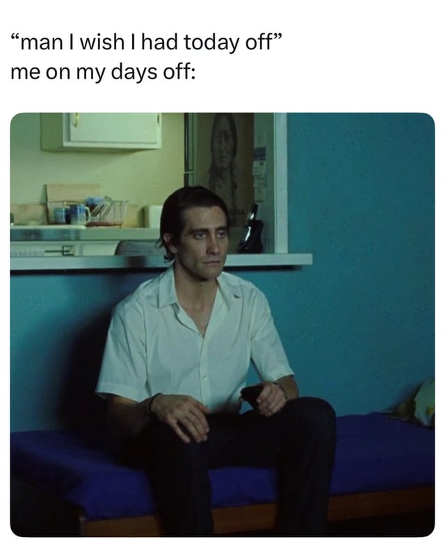 This meme contrasts the desire for a day off with the reality of boredom when having one. The top text reads 'man I wish I had today off' expressing longing for free time, followed by 'me on my days off:' introducing the image. The image shows a man (likely Anton Chigurh from 'No Country for Old Men') sitting on a blue bed in a casual room with a blue wall and kitchen area in the background. He has a neutral, slightly contemplative, and bored expression, visually representing the irony of wanting free time but feeling unfulfilled when it arrives.