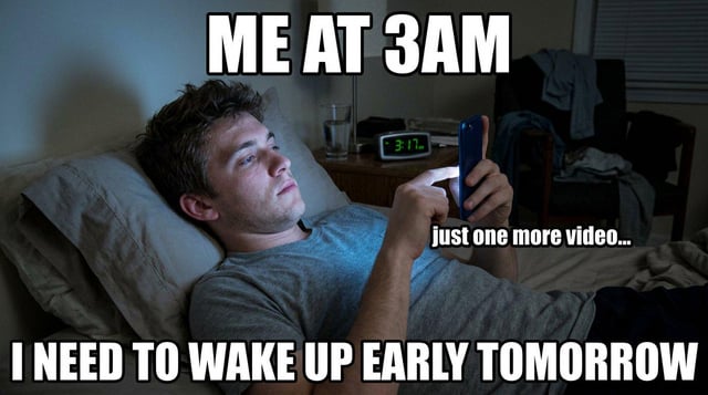This relatable single-panel meme features a young man lying propped up on pillows in a dimly lit bedroom at 3:17 AM, as shown on the digital alarm clock on his nightstand. He stares at his smartphone with a tired, glazed expression while scrolling, illuminated only by the phone's screen. Text overlays read 'ME AT 3AM' at the top, 'just one more video...' next to the phone, and 'I NEED TO WAKE UP EARLY TOMORROW' at the bottom. The meme humorously depicts the common, self-sabotaging habit of staying up late consuming online content even when fully aware of the need to wake up early the next day.