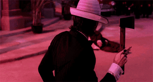 A four-frame animation showing a man in a black suit and white hat approaching another person lying injured on the ground. The man initially points a gun, then switches to holding an axe while moving toward the injured individual. The scene has a red tint and features a vintage car in the background. The animation humorously illustrates the scenario described in the title where a homeowner responds to an injured thief with an axe instead of actual first aid.