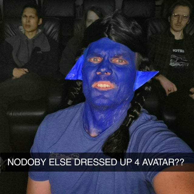 A humorous meme featuring a person who has dressed up as a Na'vi from the *Avatar* film series, with blue face paint, blue pointed ears, and braided black hair. The individual is taking a selfie in what appears to be a movie theater, surrounded by other audience members who are not in costume. At the bottom of the image, bold white text reads: 'NODOBY ELSE DRESSED UP 4 AVATAR??' (with '4' replacing 'for' as internet slang). The contrast between the person's enthusiastic cosplay and the casual, non-costumed onlookers creates a funny, relatable scenario of feeling over-prepared or out of place.