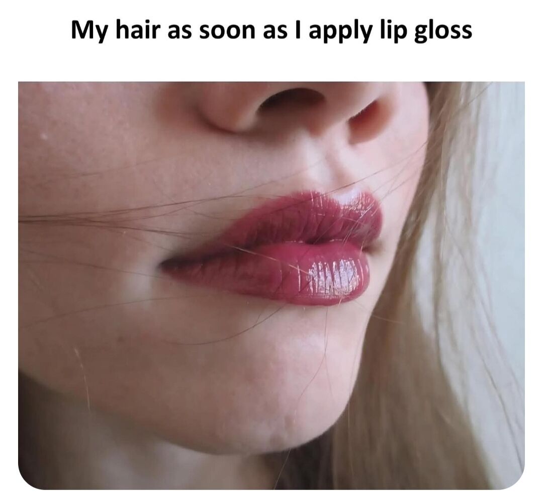 This is a single-panel relatable comedy meme. Text displayed at the top reads 'My hair as soon as I apply lip gloss'. Below the text is a close-up photograph of the lower half of a person's face, focused on their lips coated in shiny, sticky dark pink lip gloss. Multiple thin stray strands of hair are stuck directly to the wet lip gloss, visualizing the common frustrating everyday beauty routine annoyance referenced in the caption.