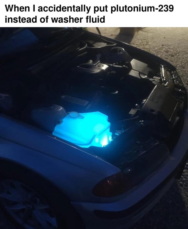 This meme features a photograph of a car with its hood open, showing the windshield washer fluid reservoir glowing a bright, unexpected neon blue. The overlaid text jokes that the person responsible for the car accidentally added plutonium-239, a radioactive chemical element, instead of regular washer fluid. The humor derives from the absurdity of confusing a highly dangerous radioactive material with a common car maintenance supply, paired with the original title joke that the glowing liquid is 'at least not green', referencing the common pop culture depiction of radioactive material as glowing bright green.