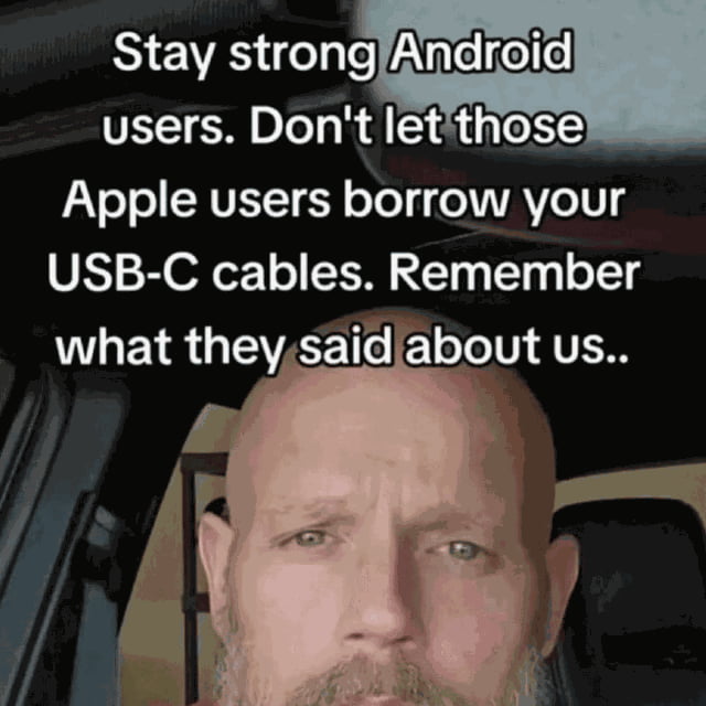 This single-panel reaction meme features a close-up of a bald, bearded man with a serious, resolute, slightly teary expression in the lower half of the frame. White text overlaid on the dark background above him reads: "Stay strong Android users. Don't let those Apple users borrow your USB-C cables. Remember what they said about us..". The joke refers to Apple's 2023 switch from their proprietary Lightning port to USB-C for iPhones, after years of Apple users mocking Android devices for using USB-C; the meme humorously encourages Android users to hold a petty grudge and refuse to lend their cables to Apple users who now need the same port they previously criticized.