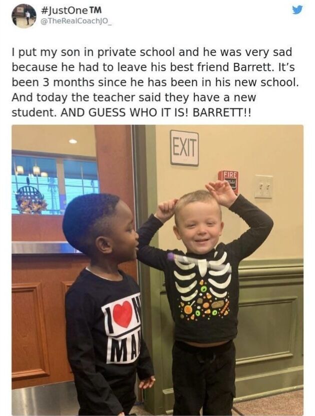 This is a screenshot of a wholesome social media post. The accompanying text explains that the poster enrolled their son in private school, leaving the boy deeply upset about having to leave his best friend Barrett. Three months after the son started at his new school, his class welcomed a new student who turned out to be Barrett. The attached photo shows two young boys in a school hallway: the poster's Black son looks happily at his friend Barrett, a white boy who is grinning widely with both hands raised near his head in obvious excitement about the reunion. An exit sign and fire alarm are visible on the wall behind the pair.