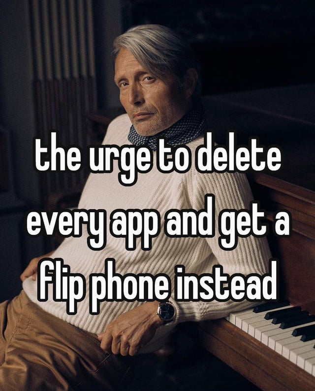 This is a relatable mood meme featuring famous Danish actor Mads Mikkelsen leaning against a wooden grand piano, with bold white text overlay across the image that states 'the urge to delete every app and get a flip phone instead'. The image conveys the quiet, widespread feeling of being overwhelmed by modern smartphone use, endless app notifications, and constant digital connectivity, expressing the common relatable desire to simplify life by switching to a low-tech simple flip phone. Mads Mikkelsen's calm, serious expression perfectly matches this genuine urge to step back from modern digital overload.