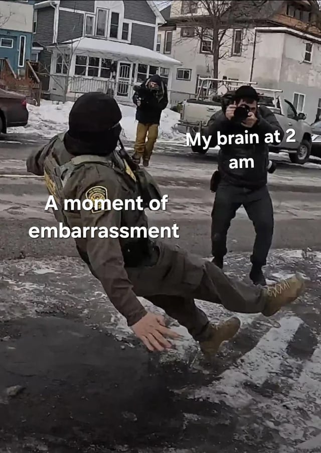 A meme featuring a real photograph of a person in a brown uniform (possibly security or law enforcement) slipping on icy ground in a snowy residential street. The individual is captured mid-fall with one leg raised and arms outstretched, appearing embarrassed. To the right, another person is taking a photograph of the moment. Text overlays are present: 'A moment of embarrassment' is positioned over the slipping person, and 'My brain at 2 am' is over the photographer. The background includes snow-covered ground, houses, a parked vehicle, and another person standing in the distance.