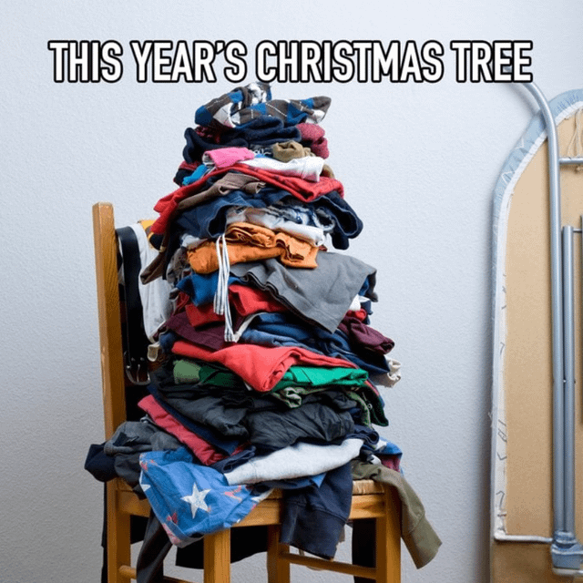 The image features a wooden chair stacked with a large, messy pile of colorful unfolded laundry (including shirts, sweaters, and various garments) arranged to humorously resemble a Christmas tree. Prominently displayed at the top in bold, capital letters is the text 'THIS YEAR'S CHRISTMAS TREE'. To the right of the chair, an ironing board is visible, emphasizing the unprocessed state of the laundry. The humor stems from the relatable scenario of neglected household chores (laundry) being jokingly presented as a holiday decoration, poking fun at procrastination during the Christmas season.