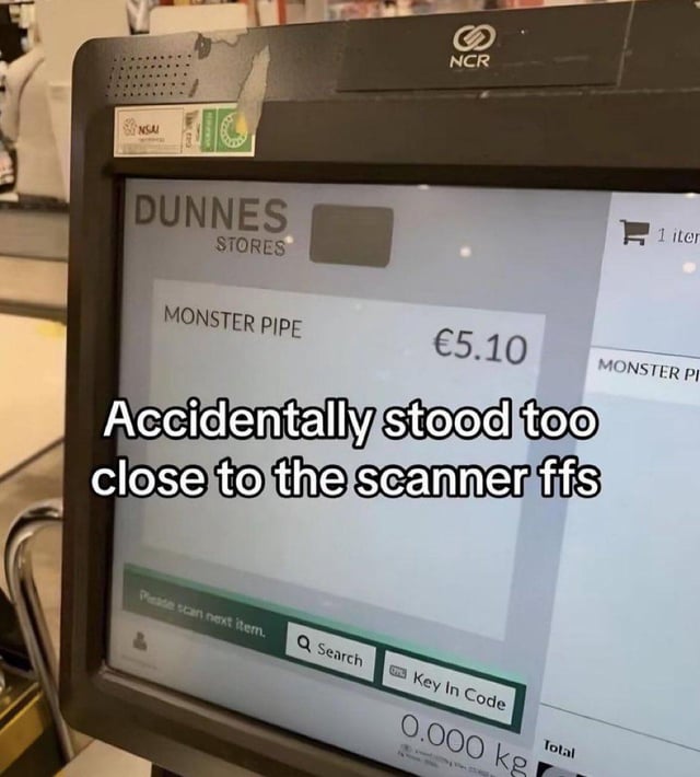 A photograph of a checkout scanner screen at Dunnes Stores displaying an item labeled 'MONSTER PIPE' priced at €5.10. Overlaid white text humorously reads: 'Accidentally stood too close to the scanner ffs', implying the scanner mistakenly identified the person as the 'Monster Pipe' product. The scanner screen shows typical retail checkout elements, including a prompt to 'Please scan next item' and a search bar. The background includes a partial view of the checkout area, reinforcing the retail setting.