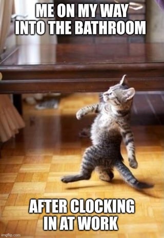 This is a relatable workplace meme featuring a small tabby kitten standing on its hind legs, walking with an exaggerated, confident swagger across a wooden parquet floor under a glass-topped coffee table. Bold white all-caps text is overlaid at the top and bottom of the image: the top text reads 'ME ON MY WAY INTO THE BATHROOM', while the bottom text reads 'AFTER CLOCKING IN AT WORK'. The joke plays on the common relatable behavior of employees going to use the bathroom immediately after arriving at work to delay starting their work tasks, humorously framing this as a priority errand the second they arrive on the job.