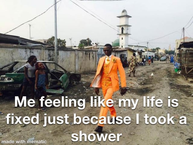 The meme features a photograph of a Black man wearing a sleek, bright orange three-piece formal suit and sunglasses, walking confidently down an unpaved, litter-strewn street in a low-income residential area. In the background, a broken-down green car, dilapidated concrete walls, simple housing structures, and a white mosque minaret are visible, along with a few other local residents including two young girls standing next to the broken car watching the man pass by. Large white overlaid text on the image reads 'Me feeling like my life is fixed just because I took a shower'. The humor comes from the stark contrast between the man's overly polished, self-assured appearance and the unkempt, chaotic environment around him, which acts as a metaphor for the common relatable feeling of believing you have all your life problems solved after completing one small basic self-care task like taking a shower.