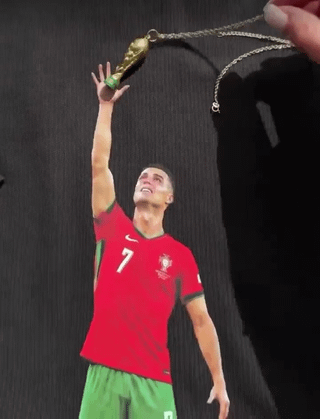 This meme uses a widely circulated photograph of professional footballer Cristiano Ronaldo, clad in the red #7 jersey of the Portuguese men's national football team, looking upward with a pained, yearning expression while extending his right hand high above his head. A person off-camera holds a small necklace shaped like the FIFA World Cup trophy just barely out of Ronaldo's reach, using forced perspective to create the visual gag that Ronaldo is attempting to grab the World Cup trophy, a major senior career title he has never won, making the joke feel intentionally cruel as noted in the original post title.