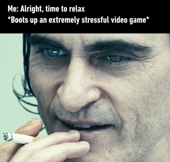 The meme consists of top text overlaid on a close-up still of Joaquin Phoenix as Arthur Fleck from the 2019 *Joker* film. The text reads 'Me: Alright, time to relax *Boots up an extremely stressful video game*'. The character shown holds a lit cigarette, with a tense, weary, strained half-smirk expression that conveys the ironic, relatable contradiction of intentionally choosing a high-stress leisure activity (like difficult, competitive video games) when the user's stated goal is to relax, a common habit among many gamers.
