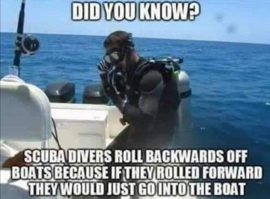 The image shows a male scuba diver in full wetsuit, oxygen tank, and diving mask standing on the edge of a small boat floating on bright blue open ocean, adjusting his breathing regulator as he prepares to dive. It uses a classic 'did you know' fake fun fact meme format: text at the top reads 'DID YOU KNOW?', while text at the bottom gives a deliberately silly, obvious explanation for why scuba divers roll backwards off boats, stating that if they rolled forward they would just go into the boat. The joke gets its humor from presenting a self-evident, common sense observation as if it is a little-known interesting piece of trivia.