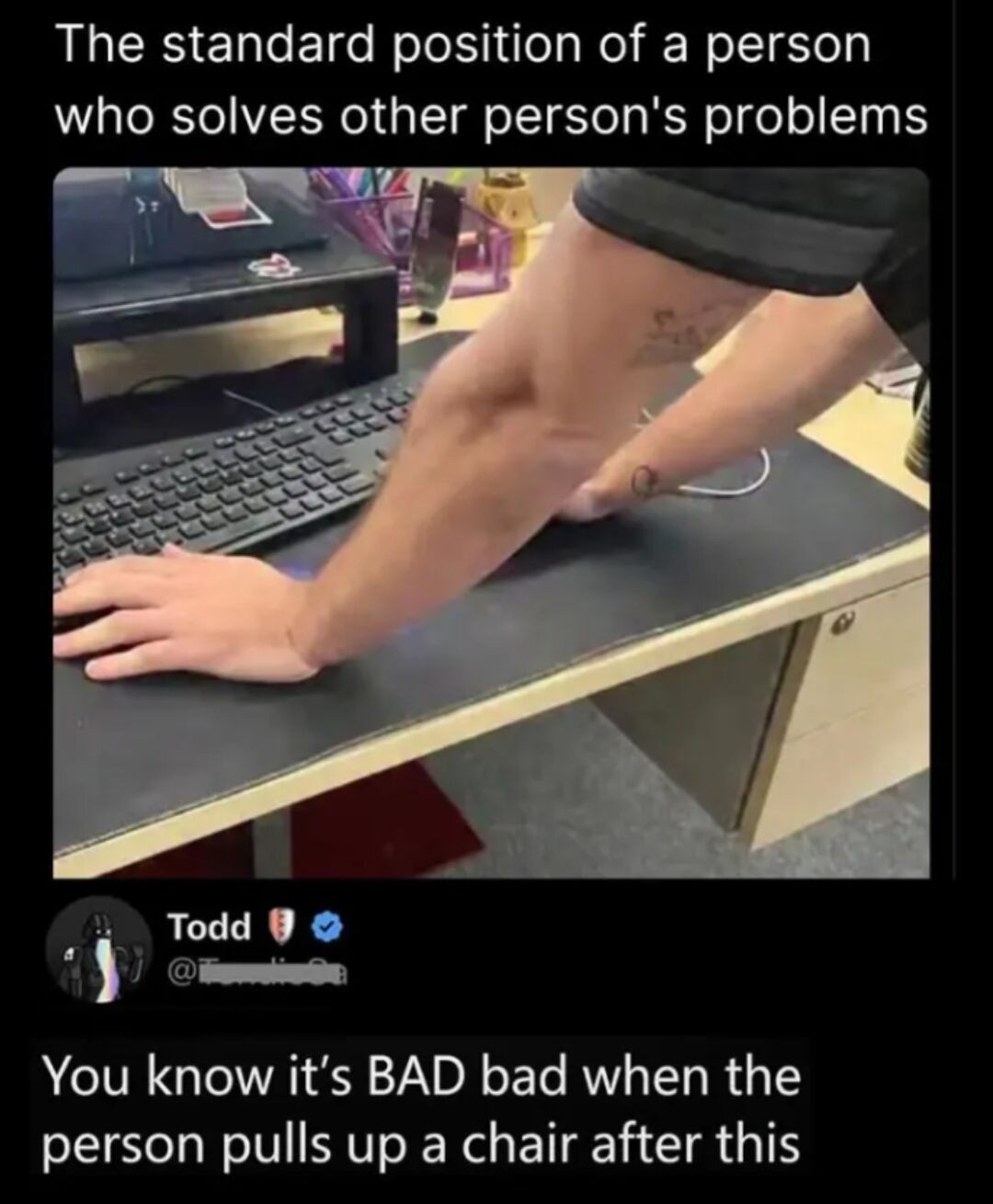 This is a screenshot of an X (formerly Twitter) post. The top caption reads 'The standard position of a person who solves other person's problems' above a photograph of a person leaning over an office desk: one hand rests on a computer keyboard, their elbow is planted firmly on the desk, and their other hand braces their own arm, in the common posture of someone intently helping another person fix a computer issue. Below the photo, a verified user named Todd comments: 'You know it’s BAD bad when the person pulls up a chair after this'. The meme humorously depicts a universally recognizable scenario of people assisting others with technical or work-related problems, with the follow-up line emphasizing that if the helper sits down, the issue is extremely severe.