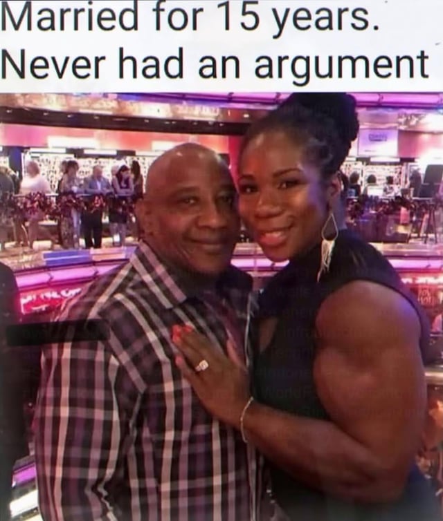 This meme features a photograph of a middle-aged man posing happily with his very physically muscular wife, who is embracing him while wearing a wedding ring. Overlaid text at the top reads "Married for 15 years. Never had an argument." The comedic implication of the meme is that the husband avoids all arguments with his wife because she is significantly stronger than him, so he would never win a disagreement if he chose to start one, which aligns with the original post title stating there are reasons he never loses an argument.