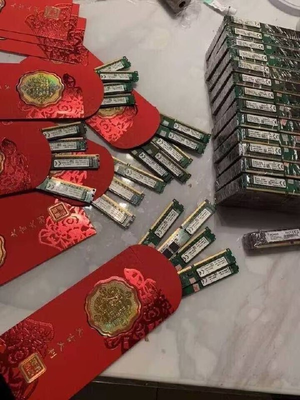 The image depicts a collection of traditional Chinese red envelopes (hongbao) placed on a marble-like surface, with DDR RAM sticks either inserted into the envelopes or scattered around them. To the right, there is a stacked pile of additional RAM sticks. The red envelopes feature classic gold and red decorative patterns, typical of those used during Chinese New Year or festive occasions. The juxtaposition of the culturally symbolic red envelopes (traditionally containing money) with modern computer RAM sticks creates a humorous and satirical commentary, possibly implying that 'tech gifts' or 'valuable tech items' are being given in place of money.