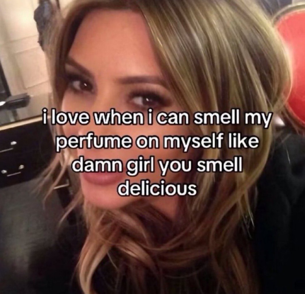 The image is a close-up selfie of public figure Kim Kardashian, who looks directly at the camera with a smug, self-satisfied expression. White text with a black outline is overlaid across the center of the image, stating "i love when i can smell my perfume on myself like damn girl you smell delicious". The meme conveys a relatable, lighthearted feeling of satisfaction when you wear a pleasant perfume and enjoy the scent on yourself, representing small, casual acts of self-appreciation.