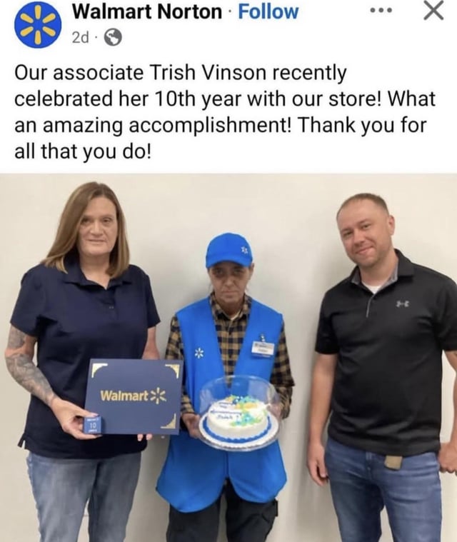 This image is a screenshot of a public social media post from the page of Walmart Norton, a physical Walmart retail location. The post text celebrates associate Trish Vinson's 10 year work anniversary with the store, framing it as an amazing accomplishment and thanking her for her contributions to the business. The photo attached to the post shows three people: a woman on the left holding a branded Walmart service certificate, Trish Vinson in the center wearing standard Walmart work attire including a blue cap and branded vest holding a small cake marking the anniversary, and a man standing to the right. The core humor and appeal of the meme comes from the stark contrast between the overly positive, celebratory tone of the post text and Trish's completely unamused, deadpan, unenthusiastic facial expression, which serves as relatable commentary on how low-wage retail workers often receive very minimal, underwhelming recognition for long tenures of employment.