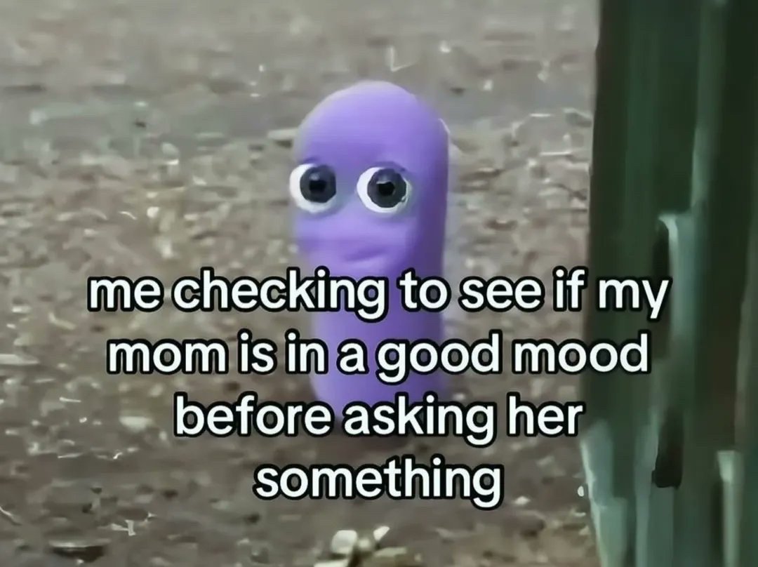 The meme displays a small, soft purple worm-shaped character with large googly eyes tentatively peeking out from a patch of dirt next to a vertical green surface, as if cautiously observing its surroundings. Overlaid on the image is text that reads "me checking to see if my mom is in a good mood before asking her something", which connects the character's shy, hesitant peeking pose to the widely relatable experience of gauging a parent's mood first to avoid rejection or scolding when making a request.