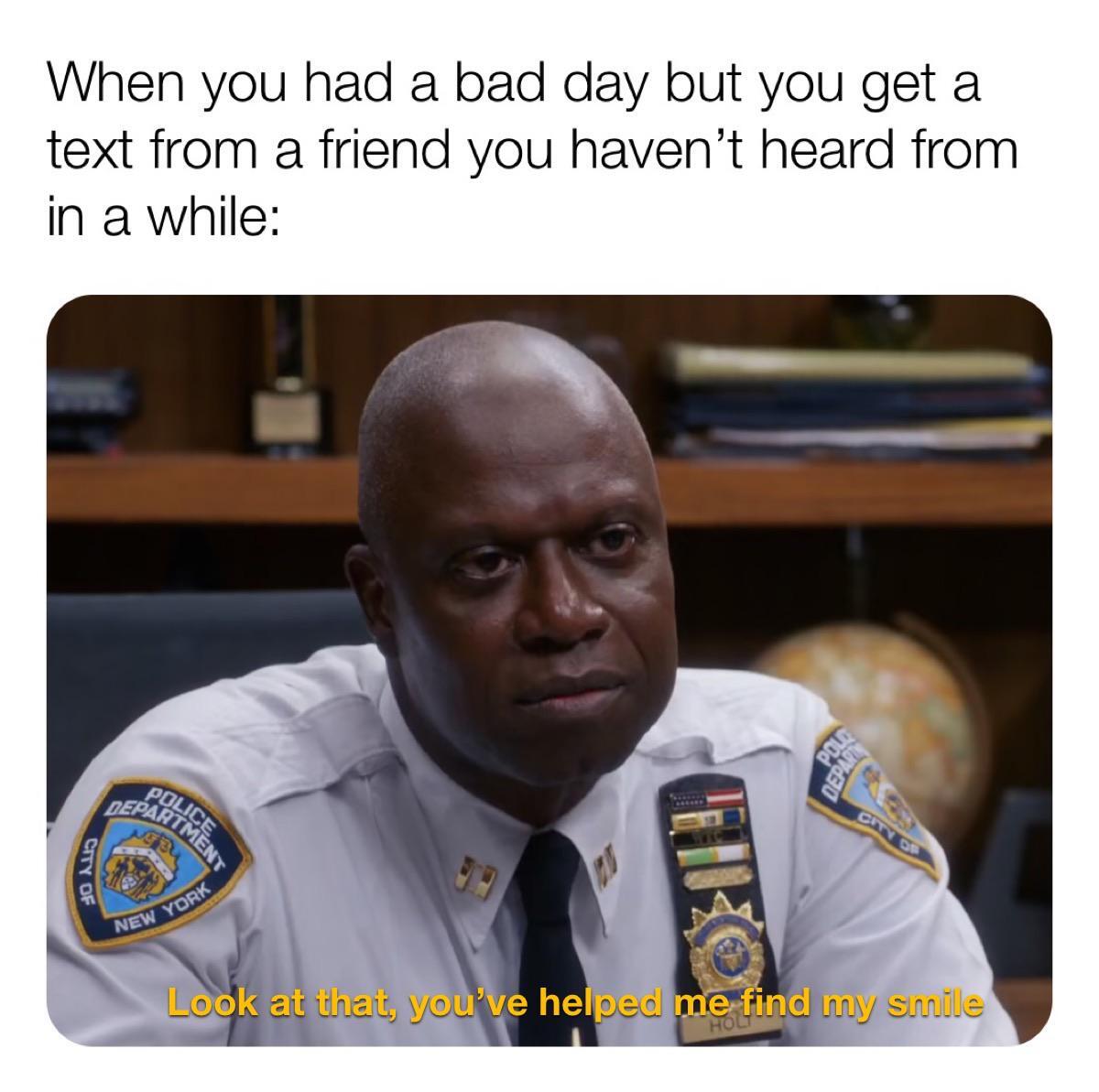 This is a wholesome relatable meme. The top text sets up a common relatable scenario: having a bad day, then unexpectedly receiving a text from a friend you have not spoken to in a long time. Below the text is a screenshot of Captain Raymond Holt, a famously stoic, emotionally reserved character from the sitcom Brooklyn Nine-Nine, wearing his NYPD uniform at his office desk. The subtitle at the bottom of the screenshot reads 'Look at that, you’ve helped me find my smile'. The humor and wholesomeness come from juxtaposing the very relatable small joy of reconnecting with an old friend with Holt's characteristic deadpan, subtle expression, making the quiet happiness feel even more relatable and heartfelt.