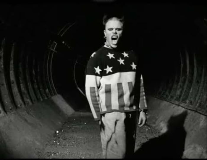 This image is a black-and-white still from Nirvana's legendary 1991 music video for *Smells Like Teen Spirit*, shared as a meme to celebrate the 30th anniversary of the band's album *Nevermind*. It features an unnamed teen extra from the video standing in a dark, narrow school hallway, wearing a sweater with an American flag design, mouth wide open in a rebellious yell. The meme highlights the enduring cultural impact of the grunge era and the iconic music video.