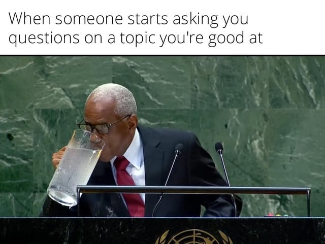 This is a single-panel reaction meme. The top of the image carries the text 'When someone starts asking you questions on a topic you're good at'. Below the text is a photograph of an older man in a formal black suit, white shirt and red tie, wearing glasses, standing at a United Nations General Assembly podium with the UN emblem visible at the bottom. He is drinking from an extremely large, almost full pitcher of water, implying he is preparing to speak for a very long time to answer all questions on the topic he is knowledgeable about. The humor comes from the relatable exaggerated reaction of being ready to ramble extensively about a subject you are passionate or well-informed on.