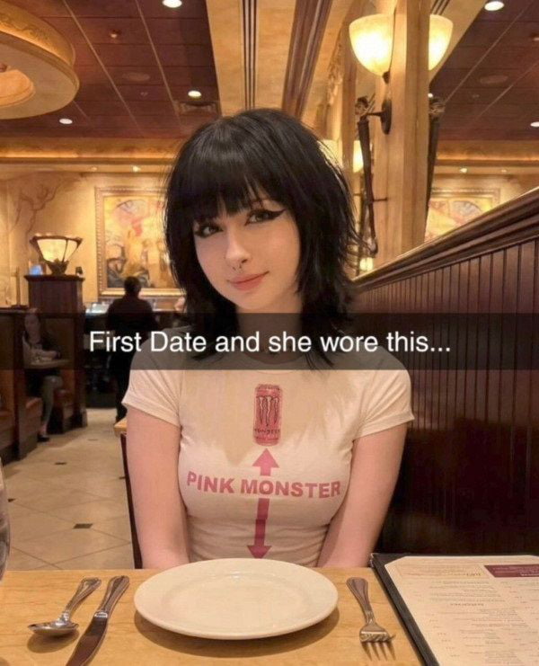 The image depicts a woman sitting at a table in a restaurant during a first date. She has shoulder-length black hair with bangs and is wearing a white t-shirt featuring a pink graphic of a canister labeled 'PINK MONSTER' with a vertical arrow. The restaurant background includes warm lighting, wooden booths, and decorative wall art. Overlaid text reads 'First Date and she wore this...', creating a humorous context around the woman's shirt choice, which is presented as notable or attention-grabbing. The original title 'I guess Imma make babies now. I have no choice.' adds a playful, exaggerated reaction to the situation, implying the date went well due to the memorable shirt.