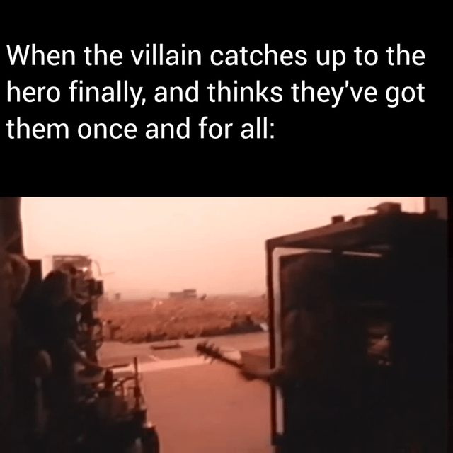 A meme composed of a text overlay and a screenshot from an unidentified movie or TV show. The top text reads: 'When the villain catches up to the hero finally, and thinks they've got them once and for all:'. Below the text is a screenshot with a reddish-orange tint, depicting a vast, arid landscape resembling a desert or battlefield, with distant structures and possibly characters, creating a tense and dramatic atmosphere typical of climactic hero-villain confrontations.
