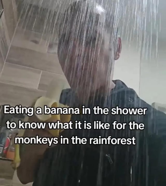 A photograph of a person standing in a shower with water pouring down over their head, holding a peeled banana. The person appears to be in the act of eating the banana. Overlaid text on the image reads: 'Eating a banana in the shower to know what it is like for the monkeys in the rainforest.' The image humorously suggests empathy by mimicking rainforest conditions (shower water as rain) while eating a banana, a food associated with monkeys.