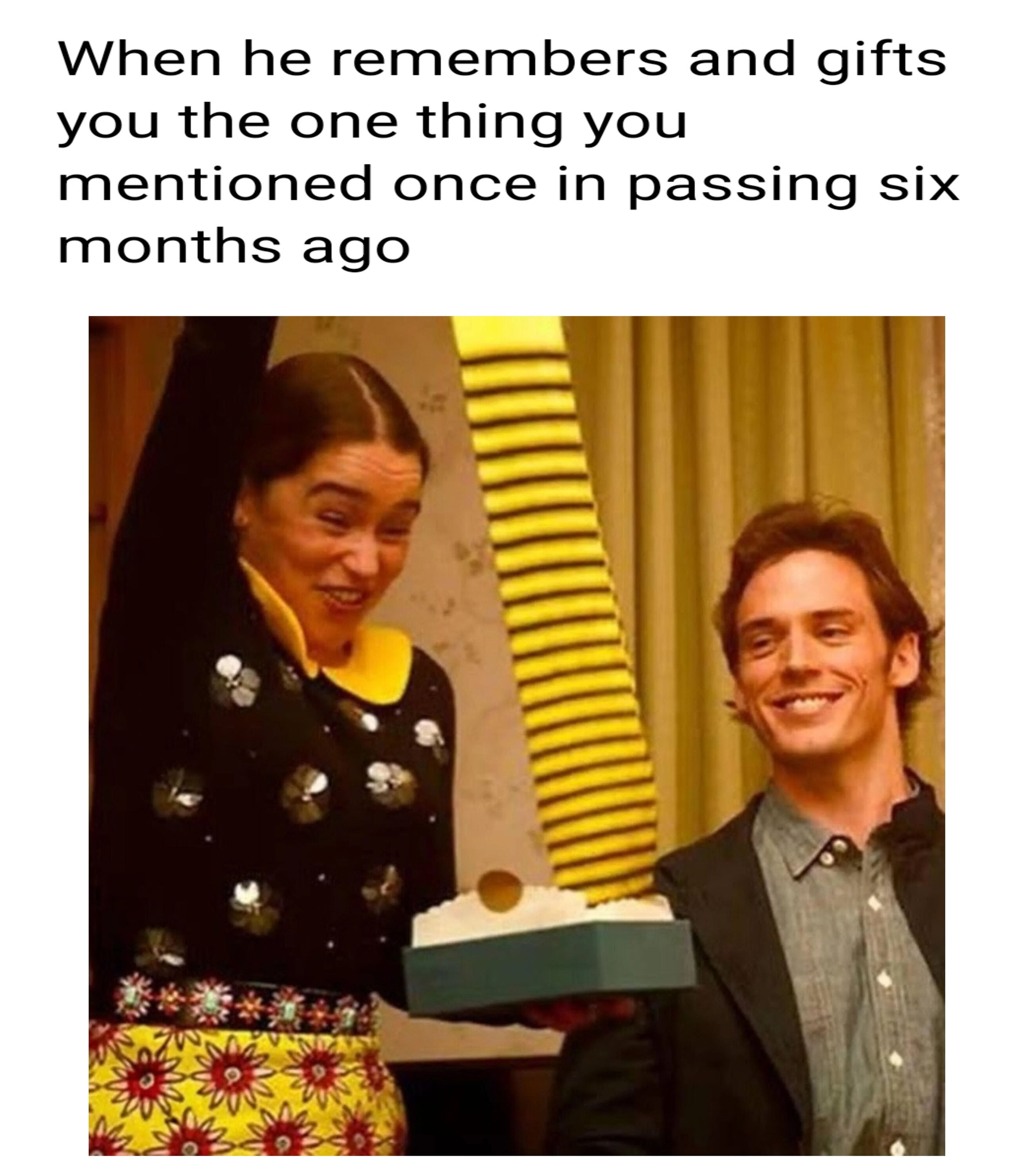 This is a single-panel wholesome relationship meme. Black text on a white background at the top reads "When he remembers and gifts you the one thing you mentioned once in passing six months ago". Below the text is a still from the 2016 romantic drama film *Me Before You*, showing Emilia Clarke as Louisa Clark looking extremely overjoyed, holding a small cake with one arm raised in celebration, while Sam Claflin as Will Traynor stands next to her smiling warmly. The meme humorously and affectionately captures the euphoria of feeling valued and seen when a romantic partner remembers small, casual comments you made long in the past.