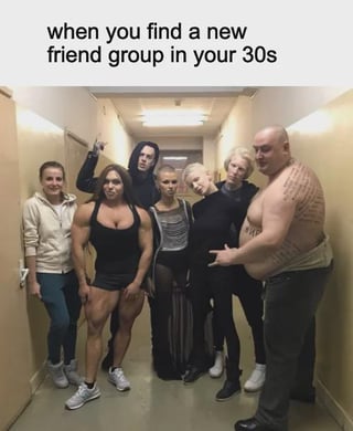 This meme features a photograph of 7 people with highly unusual, eccentric, alternative appearances posing for a group photo in a plain, narrow beige indoor hallway. The text at the top of the meme reads "when you find a new friend group in your 30s". The humor comes from the relatable observation that many people stop prioritizing fitting in with mainstream social norms once they reach their 30s, so their friend groups often consist of other uniquely odd, non-conforming people who match their authentic personalities rather than socially accepted standards of normalcy. The group includes an extremely muscular female bodybuilder, a goth person holding up a middle finger, multiple people with alternative fashion and hairstyles, and a large shirtless tattooed man leaning against the wall making a hand gesture, emphasizing the odd, non-mainstream nature of the friend group.