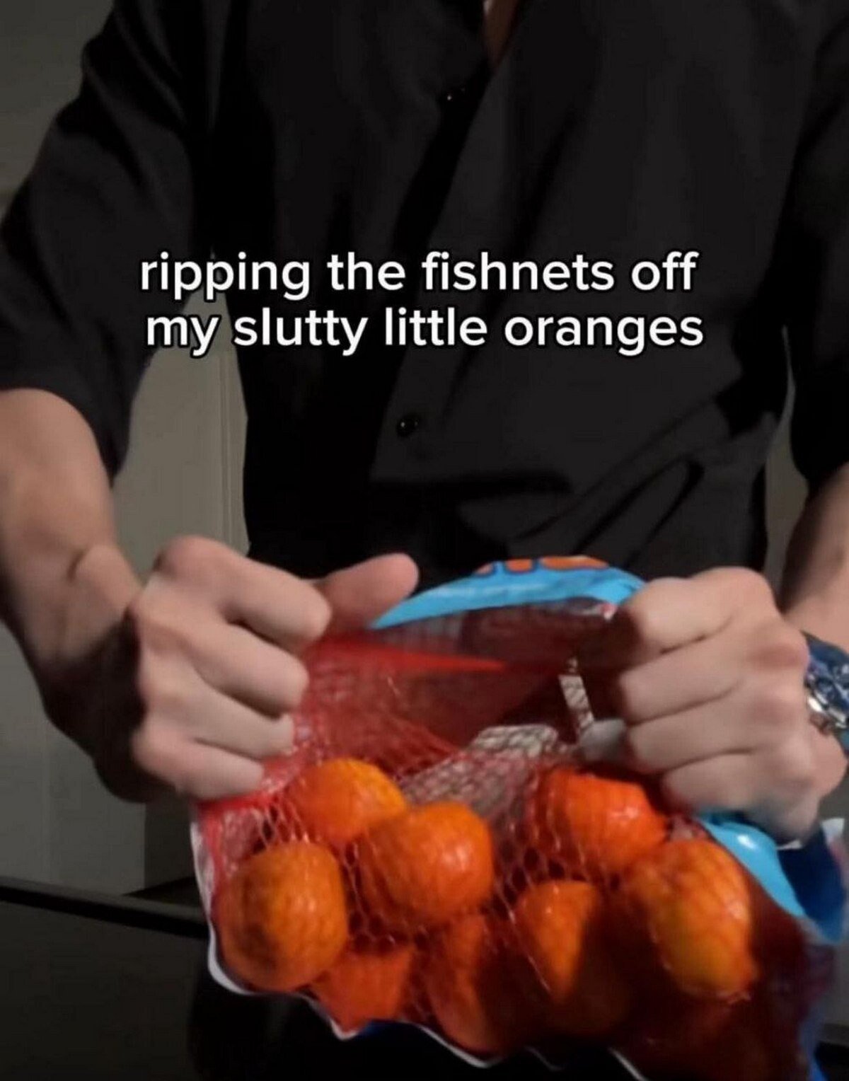 The image depicts a person wearing a black shirt, focusing on their hands as they tear open a red mesh bag (resembling fishnets) filled with small oranges. Overlaid text reads: 'ripping the fishnets off my slutty little oranges,' creating a humorous double entendre by sexualizing the mundane action of opening a fruit bag. The joke lies in the absurdity of applying provocative language ('fishnets,' 'slutty') to innocent oranges, blending everyday activity with suggestive wordplay.
