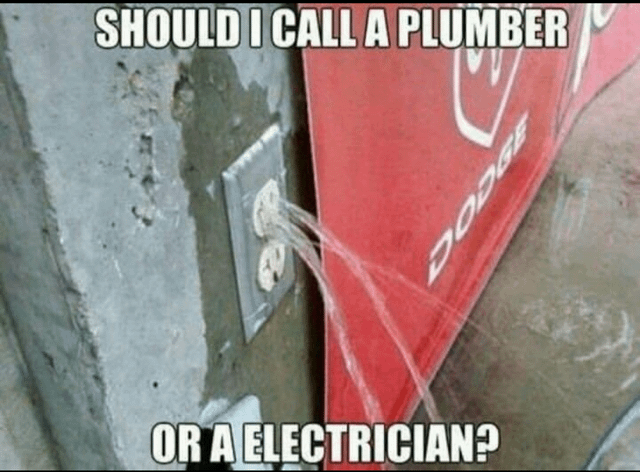 This meme shows a very unusual problem: an electrical outlet installed in a concrete wall is actively leaking water out onto a nearby red Dodge vehicle panel. The image poses a question to the viewer asking whether they would call a plumber (to fix the water leak) or an electrician (to fix the wet electrical outlet), creating a funny, confusing dilemma because the problem involves both trades. It plays on the absurdity of water leaking from an electrical fixture that should never have water inside it.