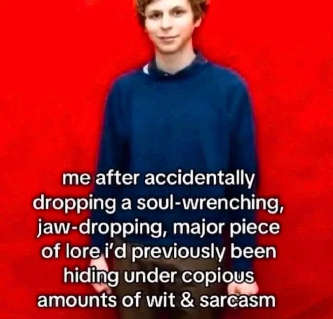 The meme features real actor Michael Cera standing against a plain bright red background, wearing a dark blue long-sleeve sweater, with his iconic deadpan, slightly awkward neutral expression. White text with a black outline is overlaid on the lower half of the image, reading "me after accidentally dropping a soul-wrenching, jaw-dropping, major piece of lore i’d previously been hiding under copious amounts of wit & sarcasm". The relatable joke describes the awkward, unreadable feeling after you accidentally share very personal, deep, or previously hidden information that you had been masking behind jokes and sarcasm, perfectly paired with Cera's neutral awkward demeanor.