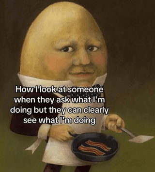 The meme features a surreal painted depiction of the nursery rhyme character Humpty Dumpty, an anthropomorphic egg dressed in a formal collared shirt with a bow tie and a white cooking apron. He is holding a small frying pan containing cooked bacon strips in one hand, and a metal spatula in the other, positioned as if he is actively cooking. His facial expression is deadpan, unamused, and slightly annoyed, directed at the viewer. White text is overlaid across the lower half of the image, reading 'How I look at someone when they ask what I'm doing but they can clearly see what I'm doing'. The joke relies on relatable frustration at being asked unnecessarily obvious questions when the answer is already visually clear to the person asking.