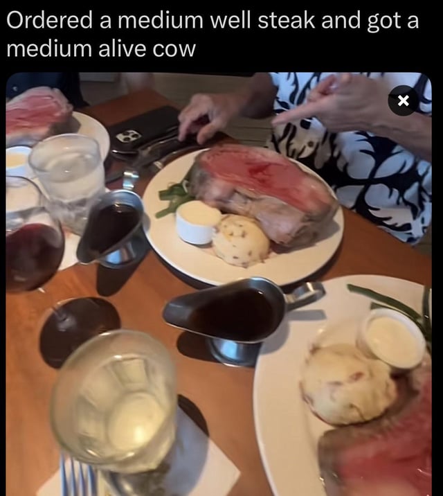 This meme features a photo of a restaurant table with plates of prime rib steaks that are extremely undercooked, showing bright red, raw-looking centers. Above the image, a caption reads 'Ordered a medium well steak and got a medium alive cow'—a playful pun that exaggerates the steak's rawness by comparing it to a living cow. A person at the table is pointing at the over-rare steak, reacting to the stark difference between the requested doneness (medium well, which should be mostly cooked with a slight pink center) and the served, nearly raw meat. The humor comes from hyperbolic wordplay, twisting the steak doneness terminology to joke that the meat is so uncooked it's practically still alive, highlighting the frustration of receiving a meal that doesn't match the order.