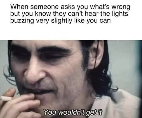 The meme features two blocks of text paired with a still of Joaquin Phoenix as Arthur Fleck from the 2019 *Joker* film, where he is holding a cigarette and wearing a weary, sardonic expression. The top text sets up the relatable scenario: when someone asks you what is bothering you, but the issue is that you can hear a faint buzzing noise coming from lights that other people cannot perceive. The bottom text, placed over the Joker's face, reads 'You wouldn't get it', conveying the feeling that this strange, specific sensory experience is too difficult to explain to people who do not have the same sensitivity, so you do not bother trying to explain why you are upset.
