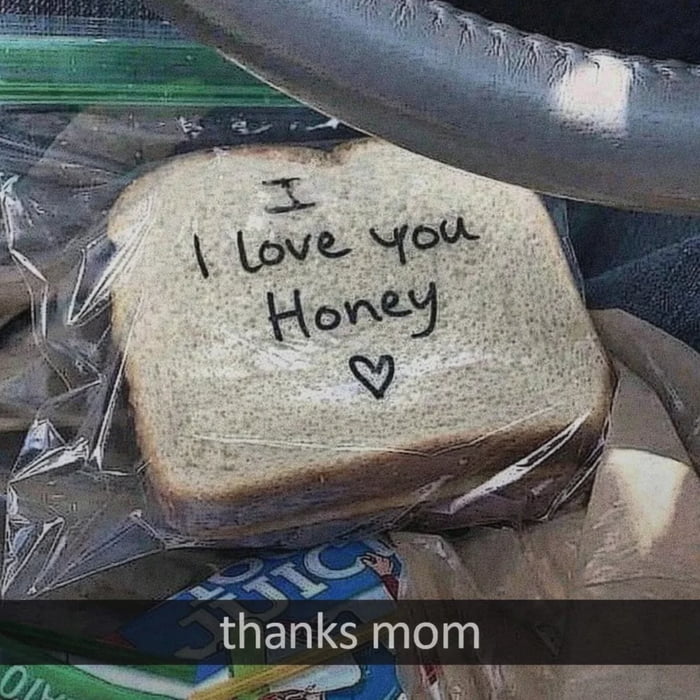 This meme features a real-life photo of a slice of sandwich bread in a plastic bag, with handwritten text that reads 'I love you Honey' followed by a small heart. A caption at the bottom says 'thanks mom'. The image was shared by a 40-year-old single man whose mother still prepares his work sandwiches; the affectionate message (with a likely playful mix-up of 'Honey' instead of his name) highlights the warm, loving bond between an adult child and their parent, creating a wholesome, relatable moment that emphasizes the comfort of parental care even in adulthood. The setting appears to be inside a car, with the sandwich resting on a lap or seat.