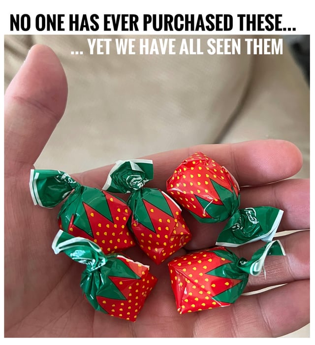 A close-up photograph of a human hand palm-up, holding five small, individually wrapped candies. The candies are encased in red and green foil with a strawberry design, featuring green triangular accents and yellow dot details. Prominent text at the top of the image reads: 'NO ONE HAS EVER PURCHASED THESE... ... YET WE HAVE ALL SEEN THEM', humorously highlighting the universal familiarity of these specific candies despite their apparent lack of consumer purchase.