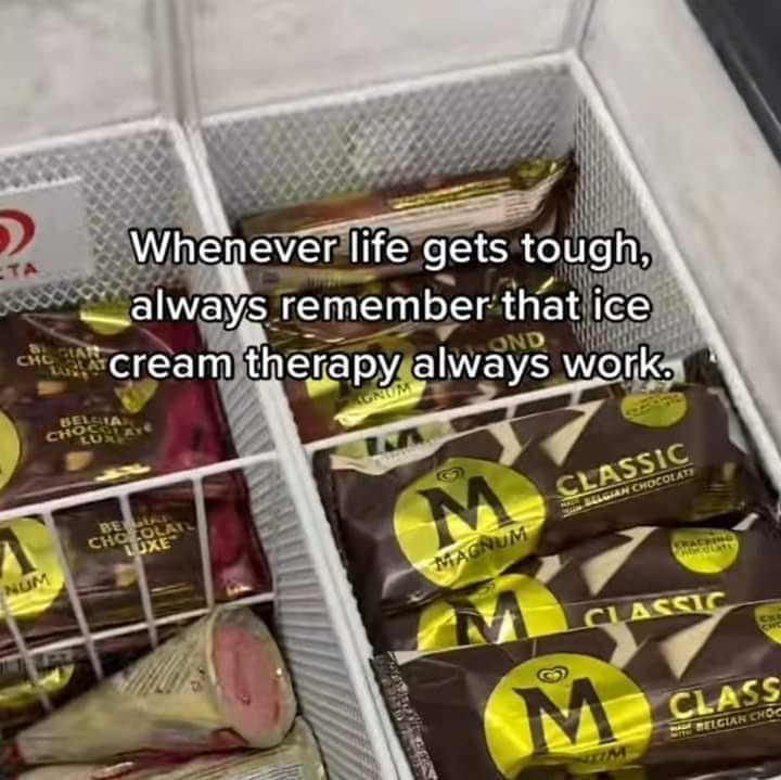 The image depicts a freezer section containing multiple Magnum ice cream bars, including flavors like 'Classic Belgian Chocolate' and 'Belgian Chocolate Luxe,' arranged in white wire baskets. Overlaid on the image is a motivational text: 'Whenever life gets tough, always remember that ice cream therapy always work.' The tone is warm and comforting, framing ice cream as a simple yet effective remedy for life's challenges. The freezer appears to be in a store, with a partial 'TA' logo visible in the top left corner, likely a store brand or label.