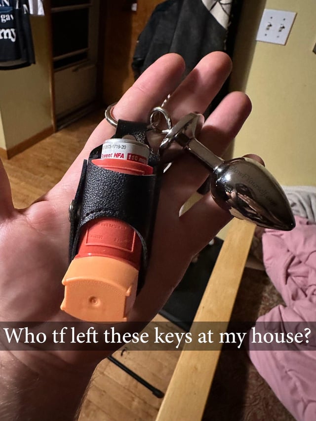 The image shows a first-person view of a person's outstretched palm holding a keyring. Instead of standard house or car keys, the ring holds two highly unusual items: a black leather holster containing an orange asthma inhaler, and a polished silver metal butt plug. White text overlaid on the bottom of the image reads 'Who tf left these keys at my house?'. The humor derives from the absurdity of referring to these personal, non-key items as 'keys', playing on the common relatable experience of finding a stranger's lost key set in your home. The unexpected inclusion of a sex toy on the keychain delivers the punchline, implying an unknown visitor left behind deeply personal, embarrassing possessions.