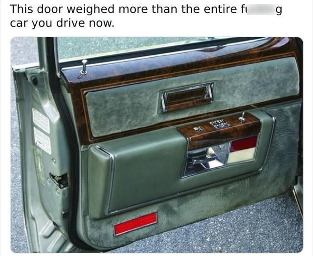 The image displays the interior side of an overbuilt vintage luxury car door, featuring thick padded grey upholstery, glossy wood grain trim, chrome hardware, built-in window controls, and a red safety reflector at the bottom. Text at the top of the meme reads, "This door weighed more than the entire f***ing car you drive now." The joke highlights the common automotive enthusiast observation that older vehicles were constructed with far heavier, more solid materials than modern lightweight, fuel-efficient cars, exaggerating the extreme mass of vintage car components for comedic effect.